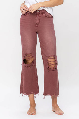 A person is wearing Livvy Dark Mauve Distressed Vintage Crop Flare Jeans by VERVET by Flying Monkey, which are high-waisted with large, shredded holes at the knees and frayed hems. The jeans are paired with a white top, and the person is barefoot. They stand against a plain white background.