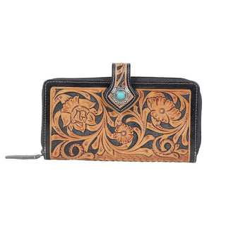 The Laken Tooled Leather Wallet by Western Edge Boutique showcases an intricate embossed floral print on its leather surface. The design is accentuated by a central turquoise gem set in the buttoned magnetic clasp. Featuring a zippered finish running along the edges, it offers both additional security and enhanced style.