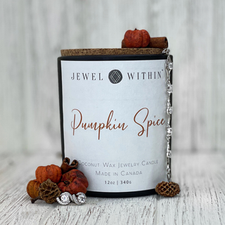 A Jewel Within Pumpkin Spice Jewelry Candle is surrounded by small decorative pumpkins, pine cones, and two pieces of 925 Sterling silver jewelry. The hand-poured coconut wax candle features a cork lid and displays "Coconut Wax Jewelry Candle Made in Canada," weighing 12oz (340g).