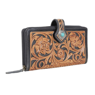 The Laken tooled leather wallet from Western Edge Boutique is a rectangular piece, intricately embossed with ornate floral patterns. The design showcases a beautiful mix of natural tan and black colors. It is equipped with a secure clasp adorned with a small turquoise stone set in silver and offers a zippered finish for added security.