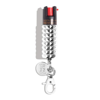 The Emergency Pepper Spray Key Ring from BLINGSTING boasts a stylish silver and black canister with a textured grip and convenient keychain attachment. The cap features a distinct red trigger, and the keychain is adorned with a small round charm displaying the brand name "BLINGSTING." Designed as part of a women's safety collection, it also includes UV marking dye for enhanced security.