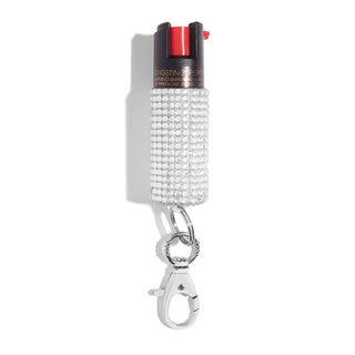 BLINGSTING's Emergency Pepper Spray Key Ring features a black and red nozzle adorned with sparkling rhinestones. It includes UV marking dye for added security and comes with a silver keychain clip for easy portability. The image is set against a plain white background.