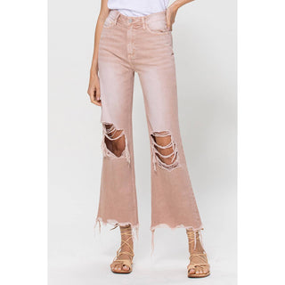 A person is modeling the Lainey Vintage Dusty Rose Crop Flare Jeans by VERVET by Flying Monkey, featuring high-waisted and flared design with distressed detail at the thighs and hem. Made from non-stretch denim, these jeans paired with a white top and beige strappy sandals create a chic look against the plain white background.