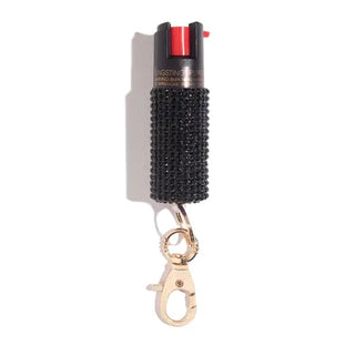 The BLINGSTING Emergency Pepper Spray Key Ring is a compact canister of pepper spray designed by a renowned women’s safety brand. It features a textured black grip and a red button on top for ease of use. For added security, it includes UV marking dye and comes with a gold keychain clip at the bottom, making it convenient to attach to your keys or bag for quick access.