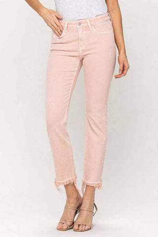 A person is wearing Krista Mid-Rise Slim Straight Jeans by VERVET by Flying Monkey, featuring a blush pink hue and cropped length with a distressed hem. Made from soft cotton, the jeans have a high waist with a button and zipper closure. The person is also wearing a white top and nude heeled sandals against a plain white background.